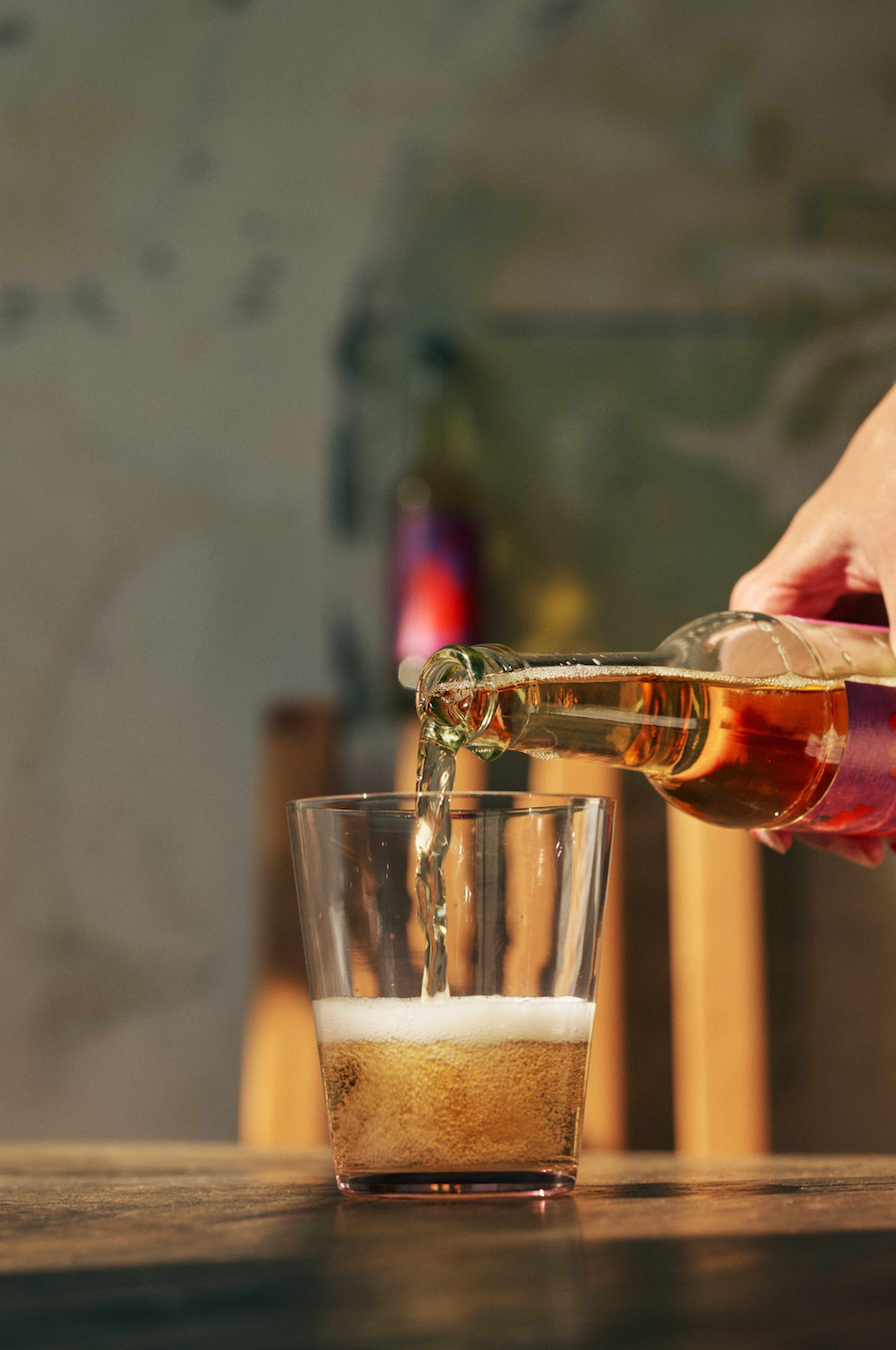 Person pouring Depanneur Organic Sparkling Rhubarb from a bottle into a glass with a blurred background