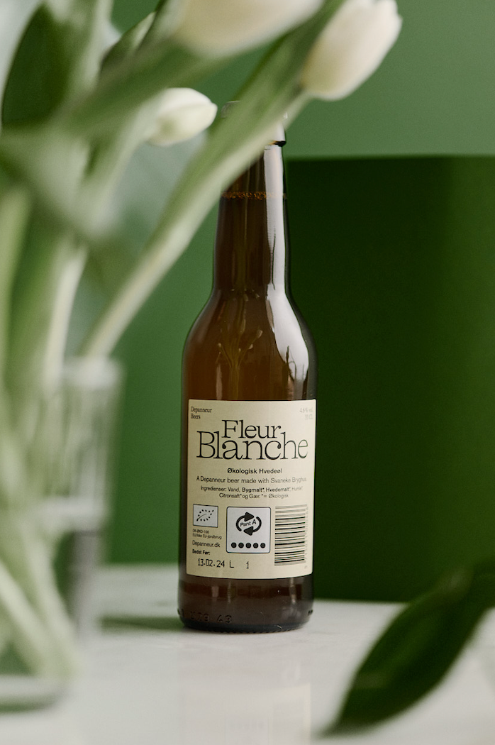 Brown bottle of Fleur Blanche organic beer with white flowers in the background