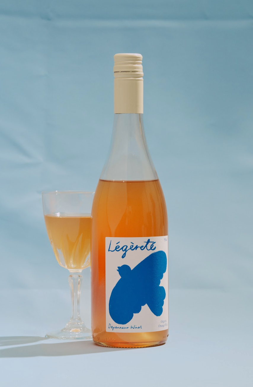 Bottle of Légèretè with a blue bird label next to a glass of the drink on a light blue background