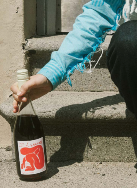 Person holding a bottle of Depanneur Organic Liebevoll red wine on concrete steps