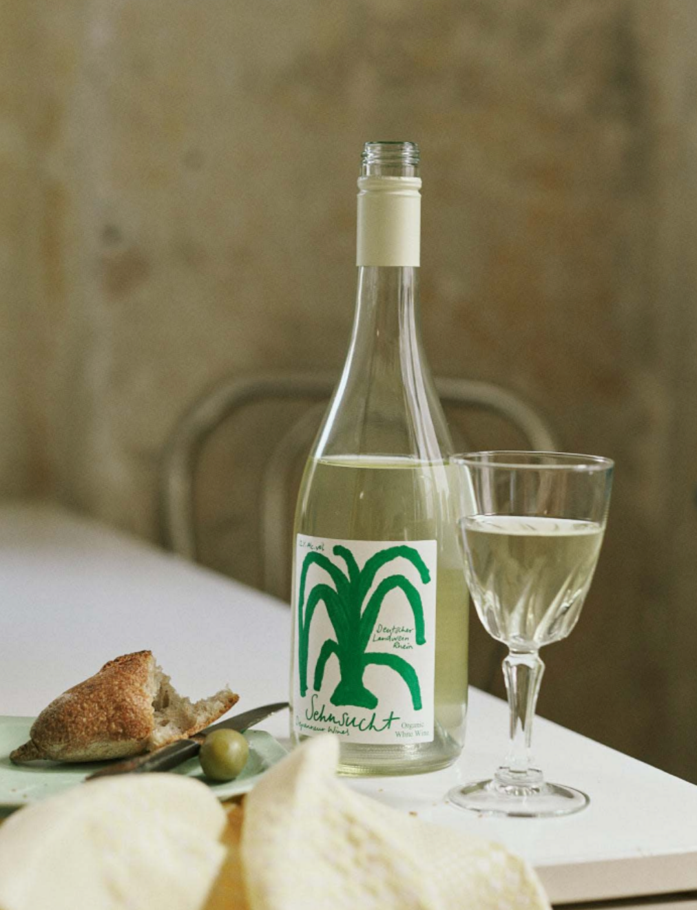 Bottle of Sehnsucht white wine with a green label next to a glass on a table.