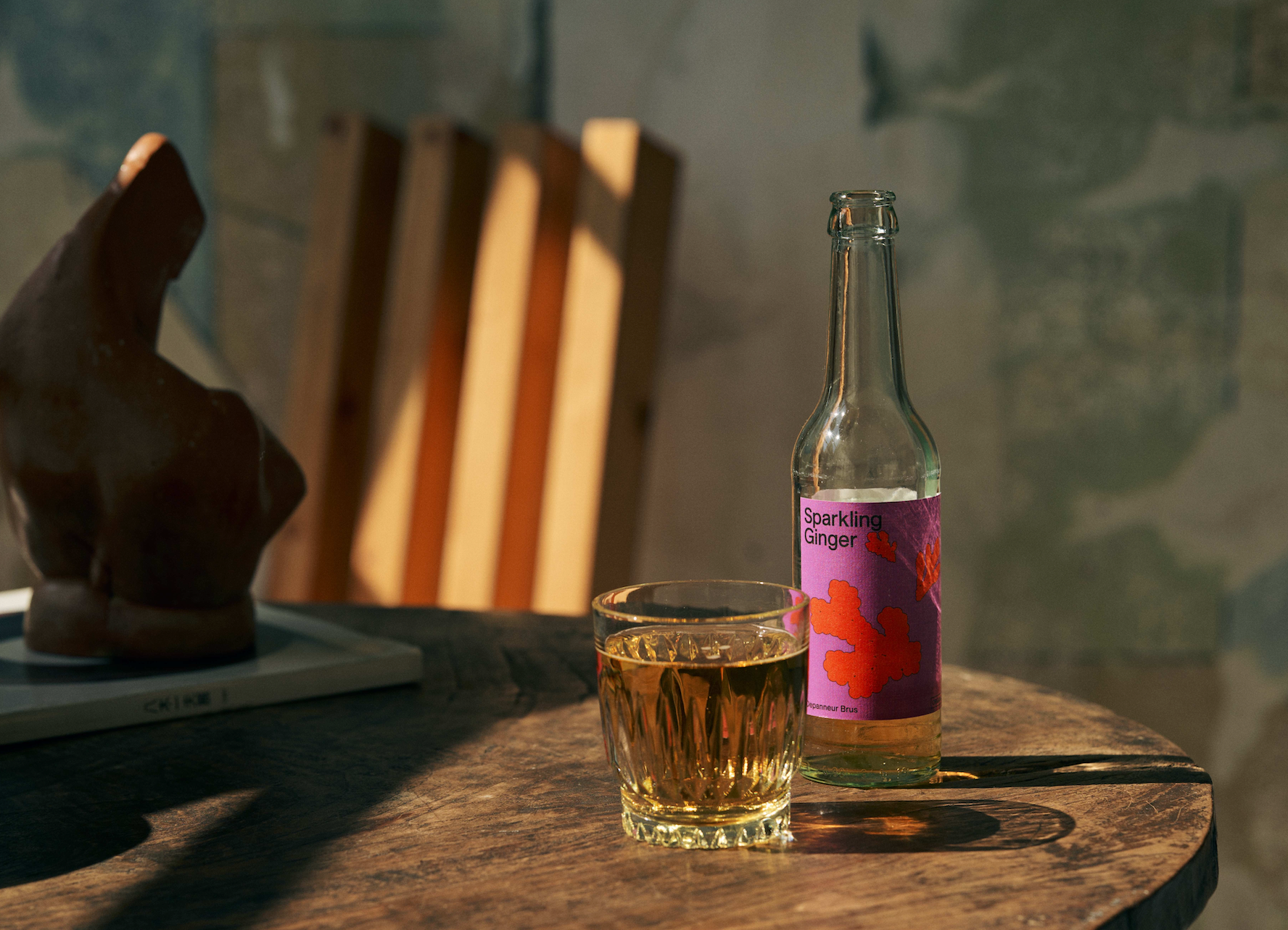Bottle of Depanneur sparkling ginger soda with a glass on a wooden table, sunlit background