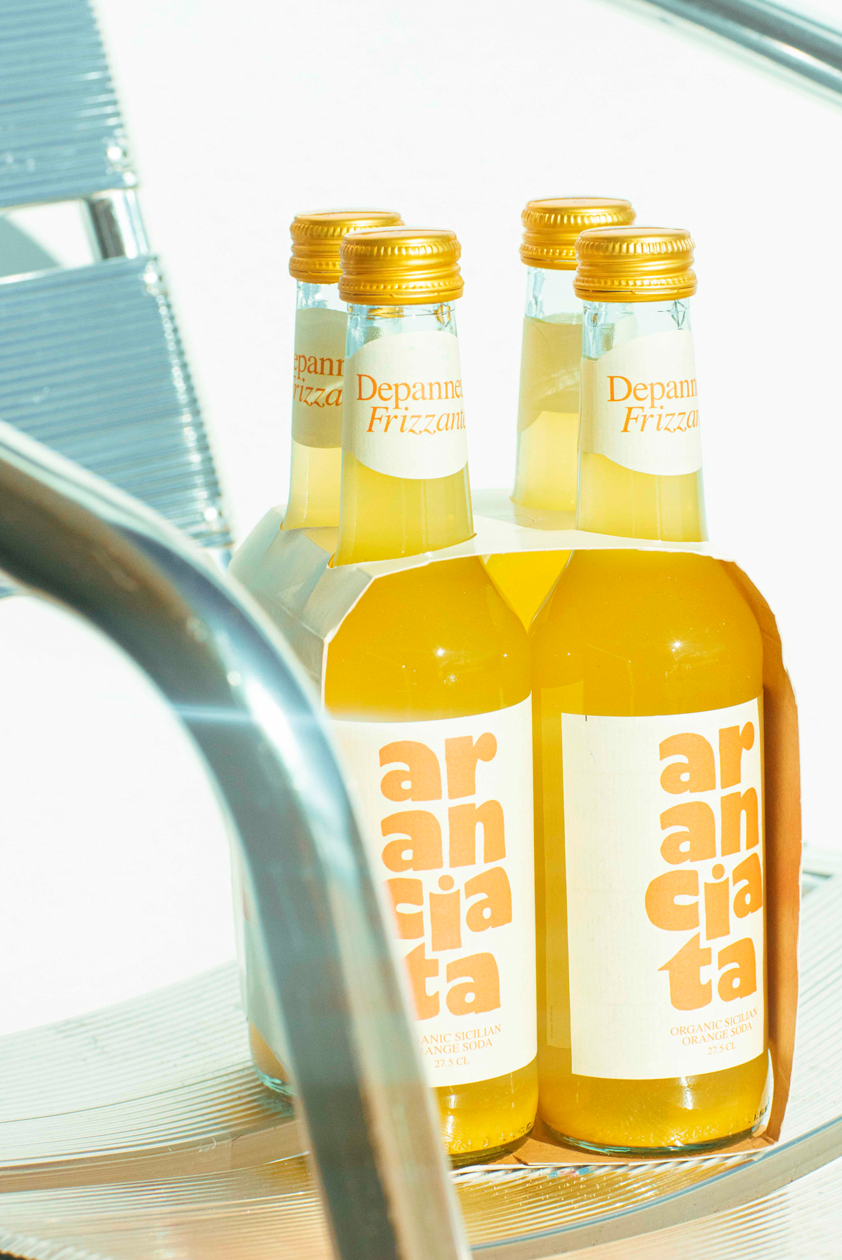 Four bottles of Aranciata organic orange soda bottles sitting on a metal chair 