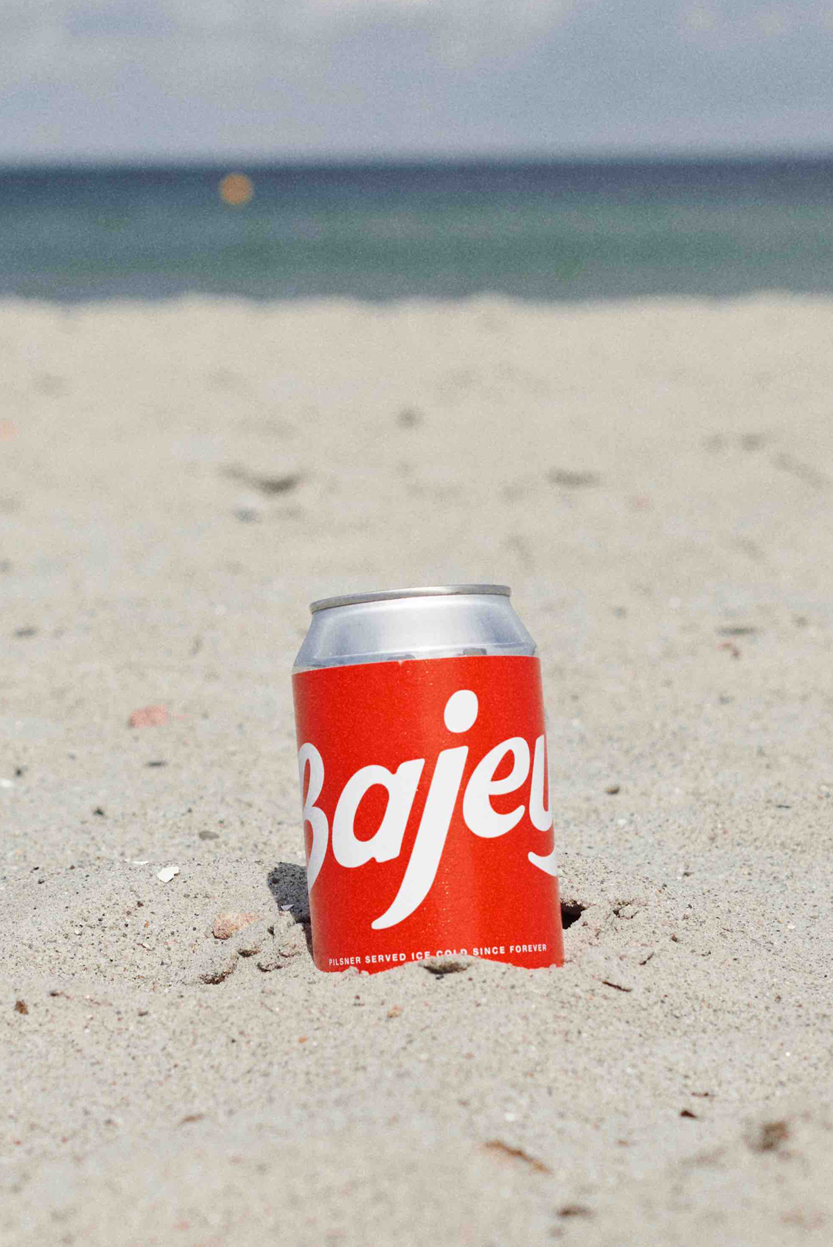 A can of Bajeur Easy Organic Pilsner on the the beach. 