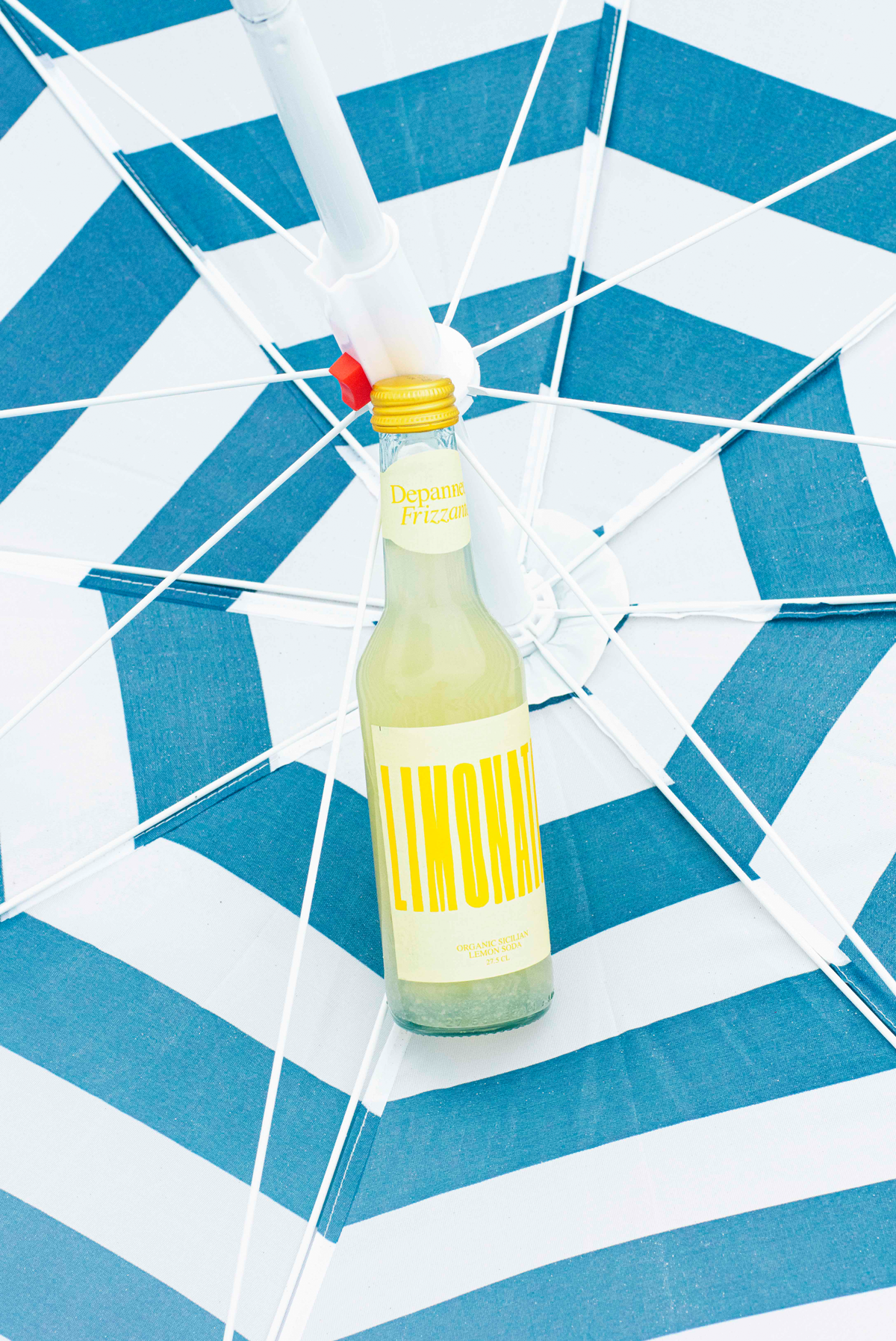 A bottle of Limonata Organic Lemon Soda laying in a beach umbrella 